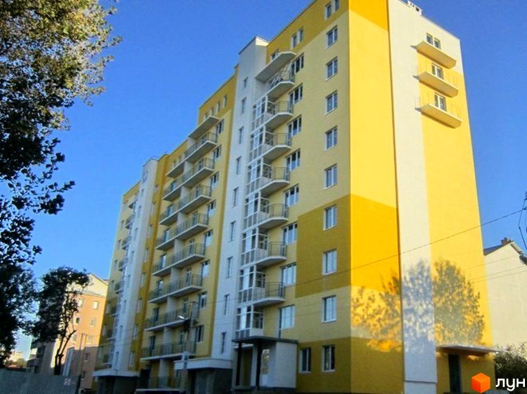 Багатоповерховий житловий будинок жовто-білого кольору з балконами. Новобудова на вул. Каховська, 27, оточена деревами.