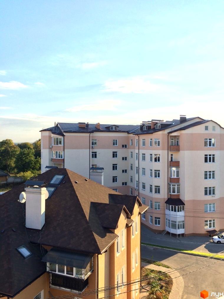 Житловий комплекс Нагірний: фасади будинків з вікнами та балконами, коричневий дах, зелені дерева та дорога.