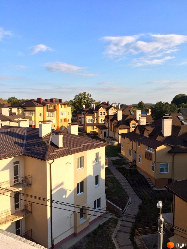 Зовнішній вигляд житлового комплексу ЖК Нагірний: світлі фасади будинків, коричневі дахи, балкони. Прибудинкова територія з доріжками та зеленими насадженнями.