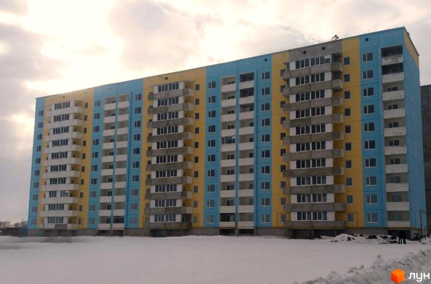 Зовнішній вигляд новобудови на вулиці Параджанова, 3. Багатоповерховий будинок з жовто-блакитним фасадом, балконами та великою кількістю вікон, на тлі хмарного неба та засніженої території.
