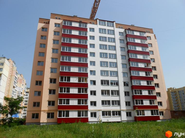 Зовнішній вигляд новобудови на вулиці Гожулівській, 30. Багатоповерховий будинок з білими та червоними фасадами, великою кількістю вікон. Навколо зелена трава.