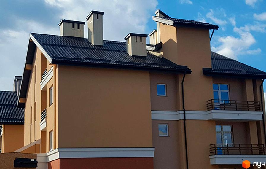 Фасад житлового комплексу Comfort Club з темним дахом та світлими стінами. На зображенні видно вікна та балкони будівлі.