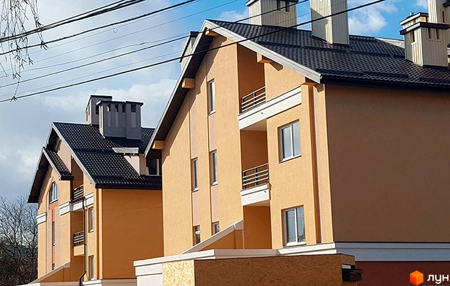 Зовнішній вигляд житлового комплексу Comfort Club з оранжевими фасадами та темними дахами. Будівля має балкони з металевими огорожами та численні вікна.