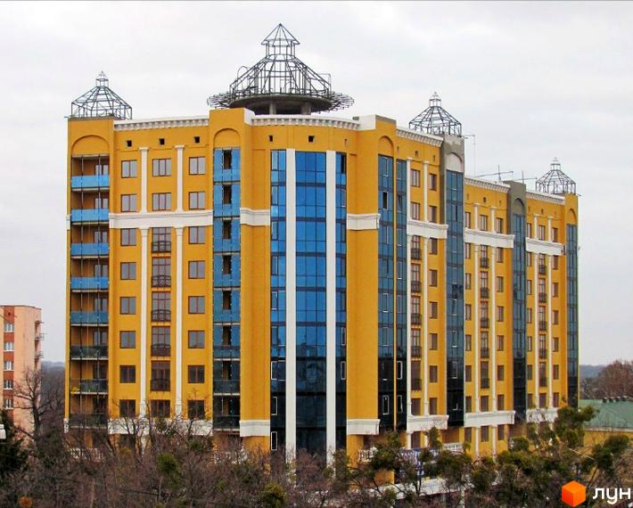 Висотна будівля жовтого кольору з синіми вікнами. На даху розташовані декоративні конструкції. Вид на фасад ЖК по вул. Івана Банка (Коваля), 2.
