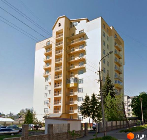 Багатоповерховий житловий будинок кремово-білого кольору з численними балконами на вул. Струтинської, 2в. Навколо розташовані дерева, вуличний ліхтар та огорожа.