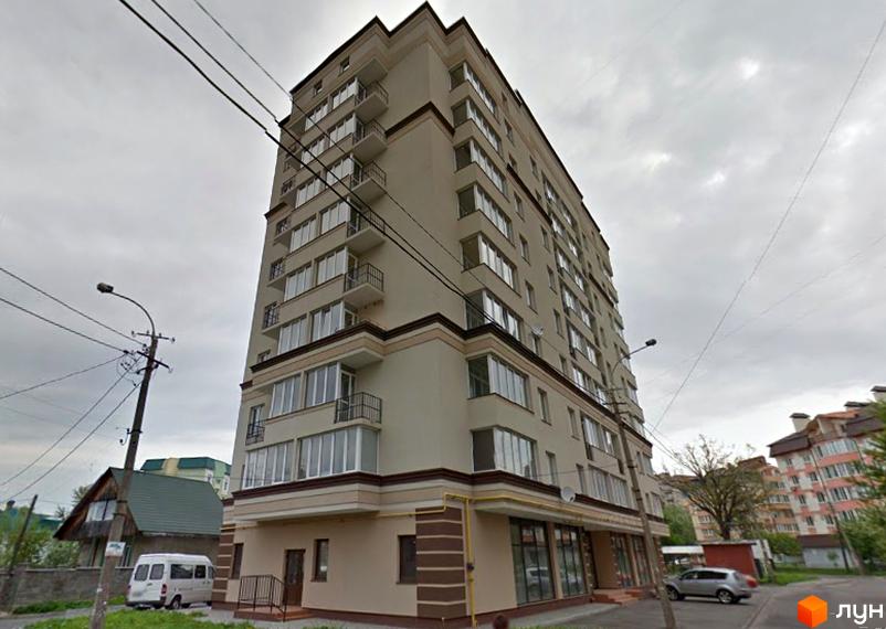 Багатоповерховий житловий будинок світлого кольору з балконами та комерційними приміщеннями на першому поверсі. Поруч вулиця та інші будівлі.