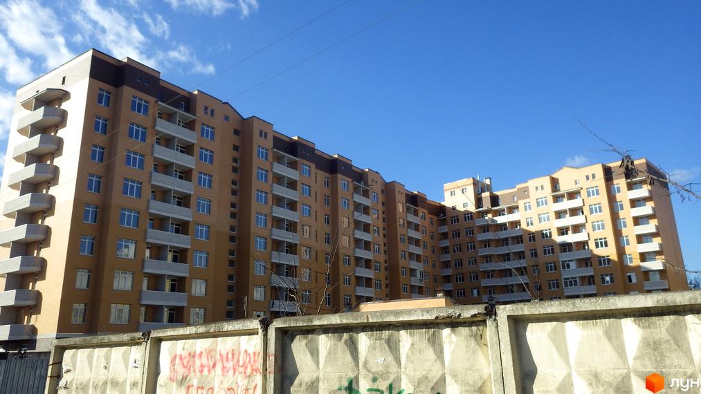 Житловий комплекс Захисник - багатоповерховий будинок з балконами та вікнами на фоні блакитного неба з хмарами. Будівельний проєкт з фасадом світло-бежевого кольору.