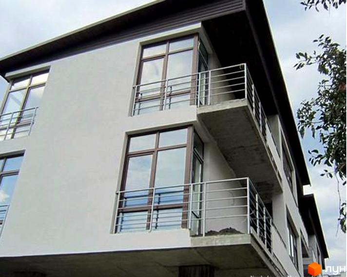 Фасад Житлового комплексу на вул. Жнивна / вул. Варшавська: світлі стіни, великі вікна з темними рамами та балкони з поручнями. Поруч видно дерева.