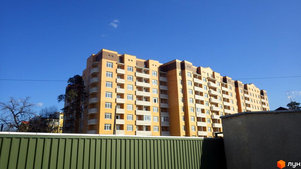 Житловий комплекс Захисник – багатоповерховий будинок з жовтим фасадом та численними балконами на тлі блакитного неба. Зелений паркан на передньому плані.