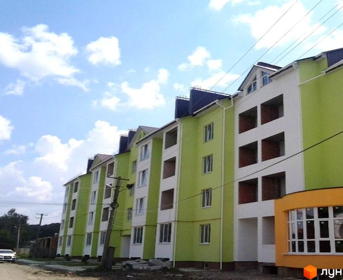 Житлові будинки з салатовими та білими фасадами під синім небом. На передньому плані дорога та елементи прибудинкової території біля вул. Заводська, 58.