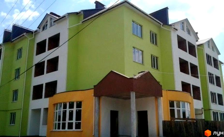 Багатоповерховий житловий будинок салатового та білого кольорів з темним дахом та помаранчевим цоколем. Видно вікна та незавершені отвори, а також вхідну групу з колонами.