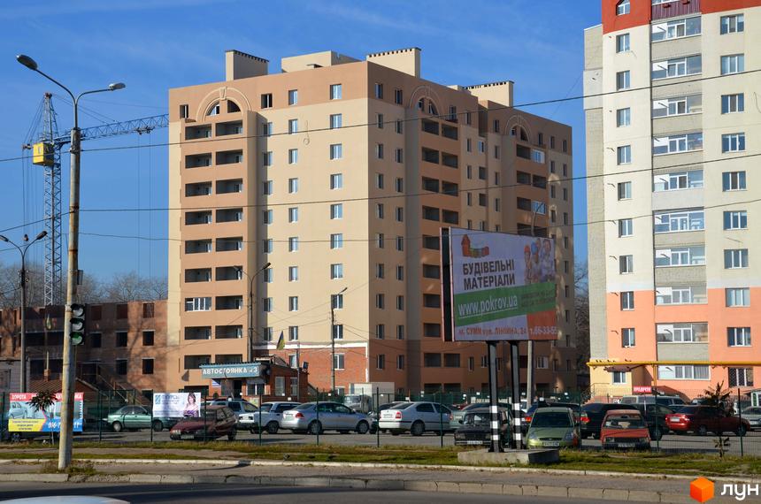 Житловий комплекс на просп. Свободи: багатоповерховий будинок бежевого та коричневого кольорів з балконами. Поруч вулиця з авто та рекламний щит.