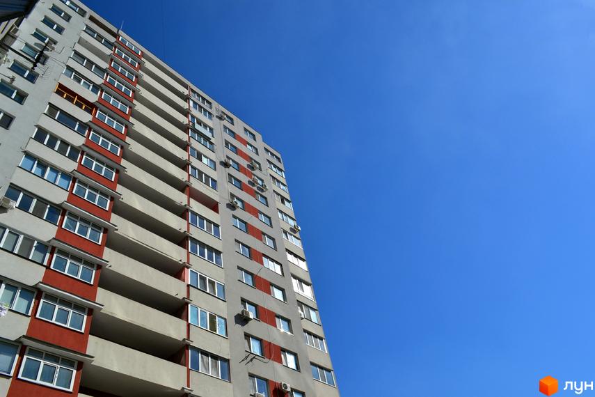 Багатоповерховий житловий будинок Житлового комплексу Пушкіна з сірим фасадом, червоними вставками та численними балконами під чистим блакитним небом.