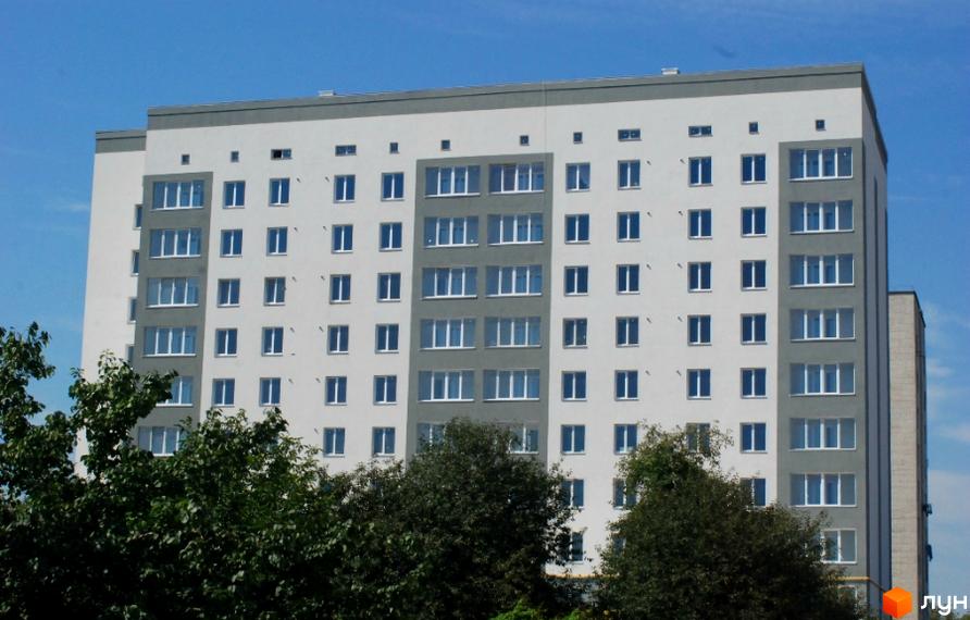 Фасад житлового комплексу Родинний з численними вікнами та сірими вставками. Навколо будівлі зелені дерева.