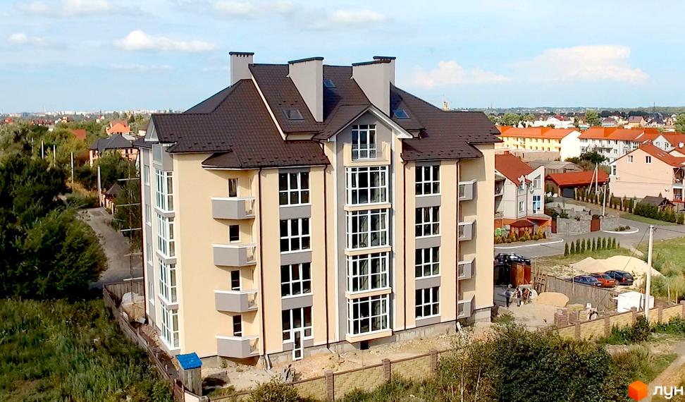 Зовнішній вигляд житлового комплексу Гостинний дім з балконами та великими вікнами. Навколо будинку зелені насадження та сусідні будівлі.