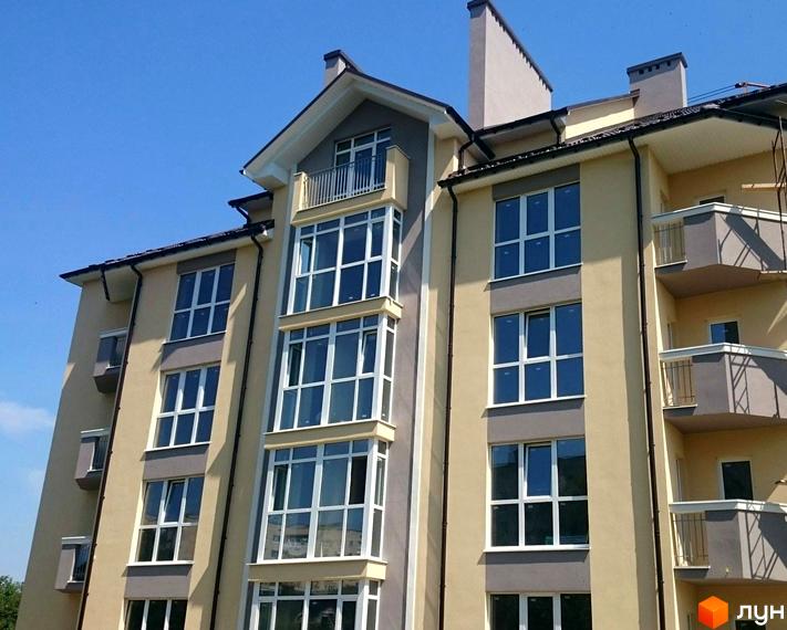 Фасад житлового комплексу Гостинний дім з великими вікнами та балконами. Зовнішній вигляд новобудови під блакитним небом.