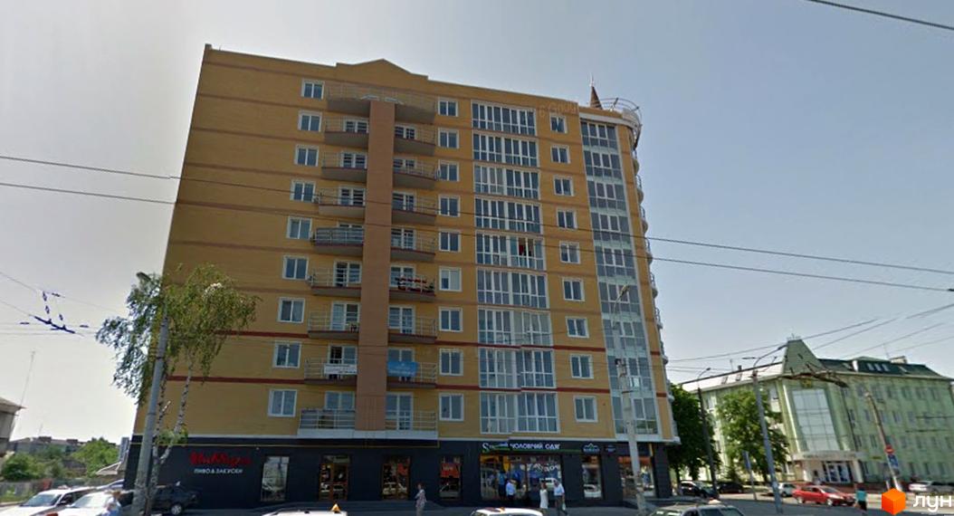 Житловий комплекс Небос Хилл – висотна жовта будівля з численними балконами та великими вікнами. Поруч зелені дерева та інша міська забудова.