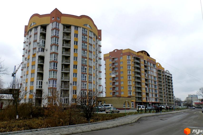 Житловий комплекс Оболоня-парк - двоповерхові будинки з жовто-коричневими фасадами та балконами. Поруч дорога та тротуар.