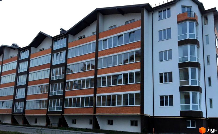 Зовнішній вигляд багатоповерхового житлового комплексу Гарантія з цегляним фасадом та великою кількістю вікон. Навколо будинку видно елементи прибудинкової території.