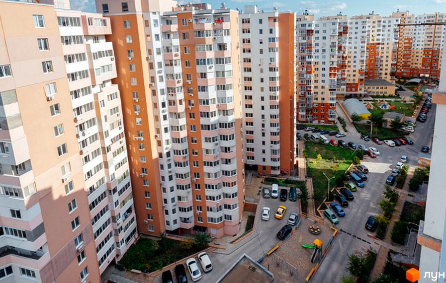 Житловий комплекс Райдужний: багатоповерхові будинки з балконами та кондиціонерами, упорядкована прибудинкова територія з дитячим майданчиком та парковкою.