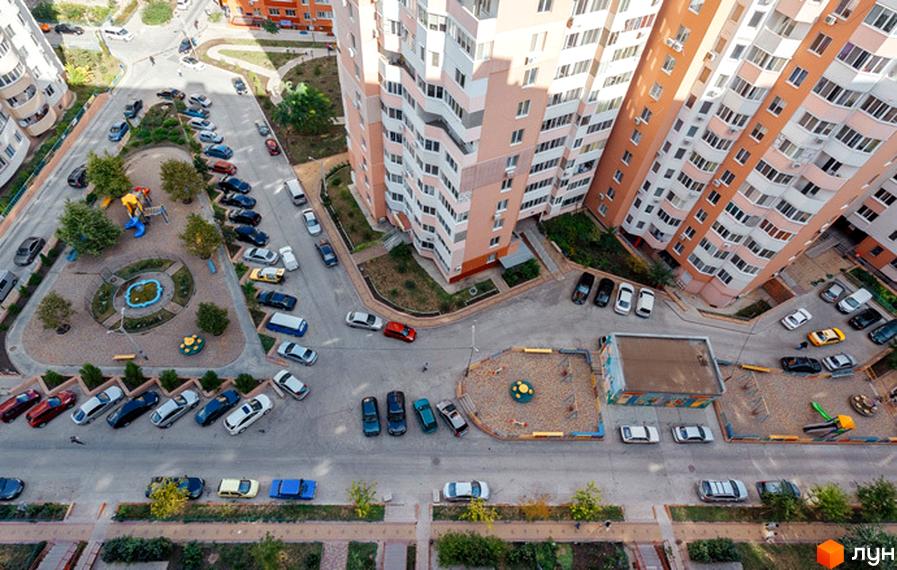 Житловий комплекс Райдужний: багатоповерхові будинки з рожевим фасадом та прибудинкова територія з дитячими майданчиками та парковкою.