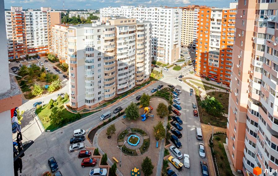 Вид на житловий комплекс ЖК Райдужний з висоти пташиного польоту. Багатоповерхові будинки з різнокольоровими фасадами та прибудинкова територія з дитячим майданчиком та парковкою.