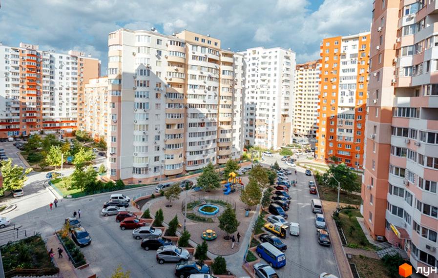 Житловий комплекс Райдужний: багатоповерхові будинки з балконами та кондиціонерами, упорядкована прибудинкова територія з дитячим майданчиком та парковкою.