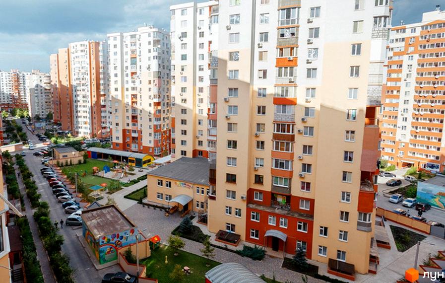 Житловий комплекс Райдужний: багатоповерхові будинки з різнокольоровими фасадами та прибудинкова територія з дитячим майданчиком та парковкою.