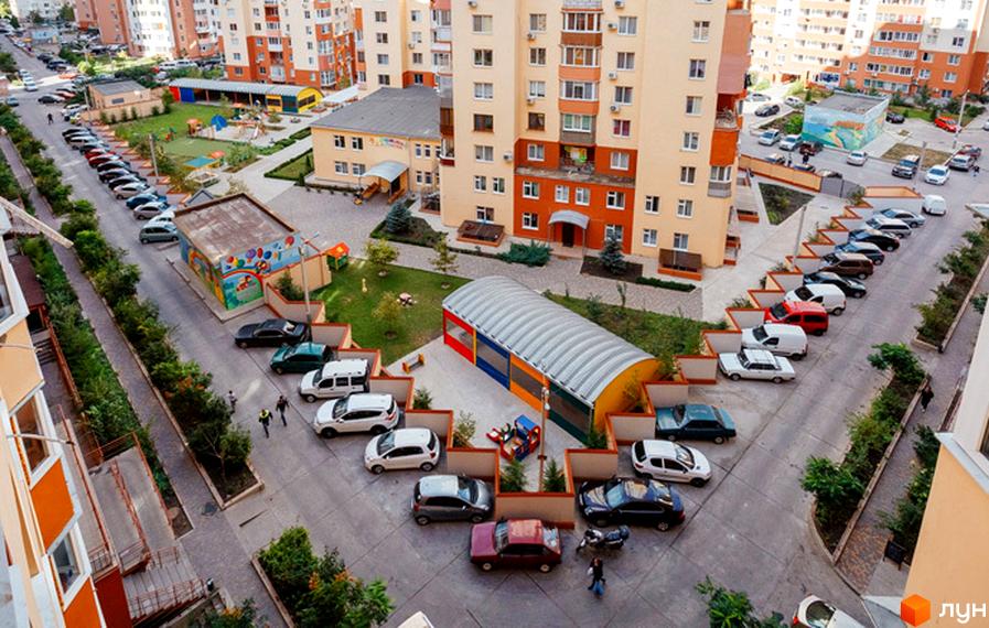 Житловий комплекс Райдужний: багатоповерхові будинки з яскравими фасадами та прибудинкова територія з дитячим майданчиком та парковкою.