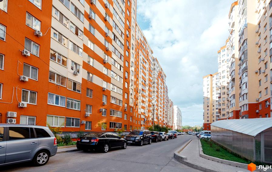 Житловий комплекс Райдужний з помаранчево-білими фасадами та кондиціонерами на стінах. Прибудинкова територія з автомобілями та зеленою зоною.