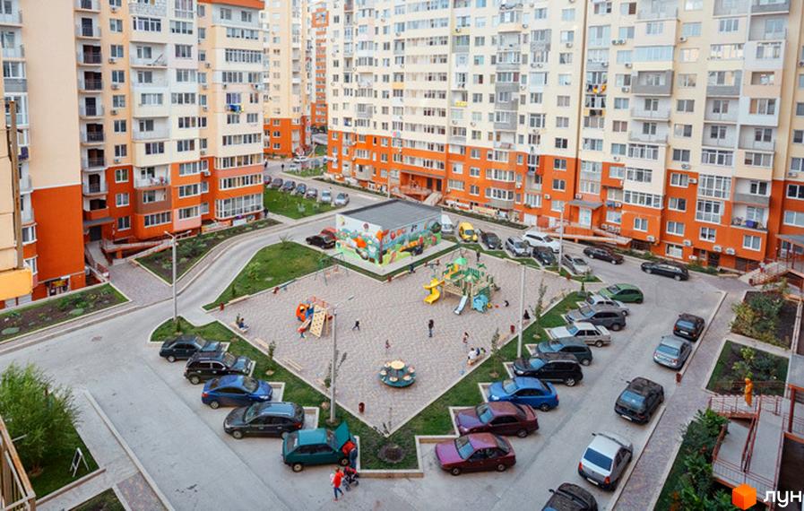 Житловий комплекс Райдужний: багатоповерхові будинки з помаранчевими та бежевими фасадами, дитячий майданчик та паркування автомобілів.