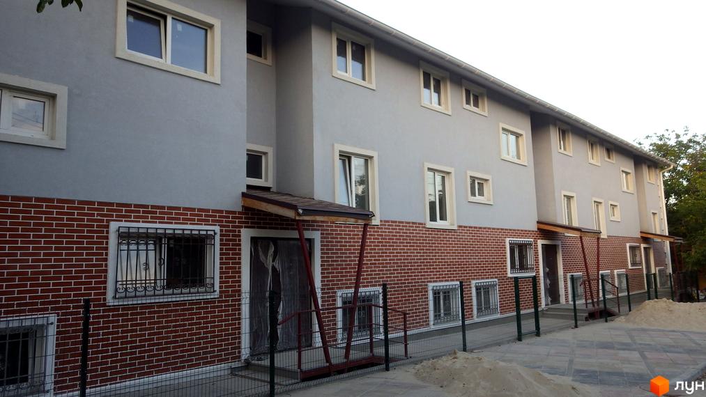 Зовнішній вигляд новобудови ЖК Голосіївські сади з цегляним фасадом та сірим оздобленням. Прибудинкова територія з піском та огорожею.