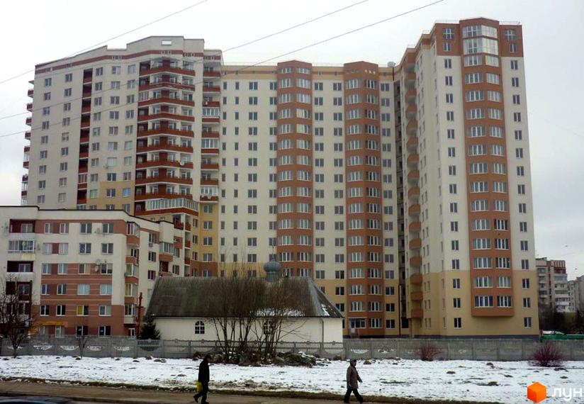 Багатоповерховий житловий комплекс на вул. Панча, 18б зі світлим фасадом та коричневими балконами. На передньому плані засніжена територія та невелика будівля з куполом.