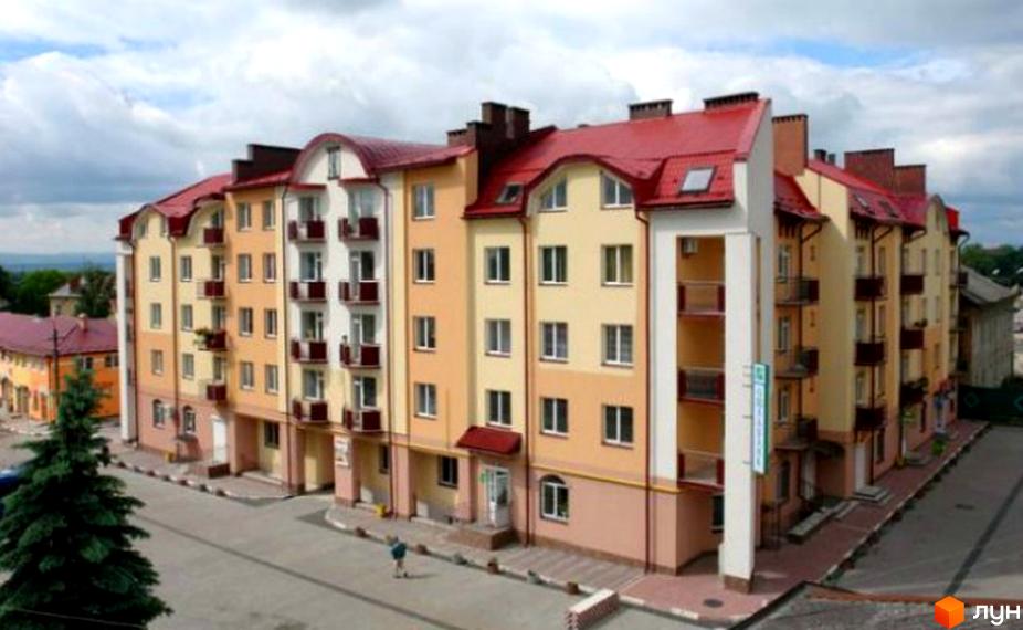 Фасад новобудови на вул. Шевченка, 5, з балконами та червоним дахом. Прибудинкова територія з деревами та дорогою.