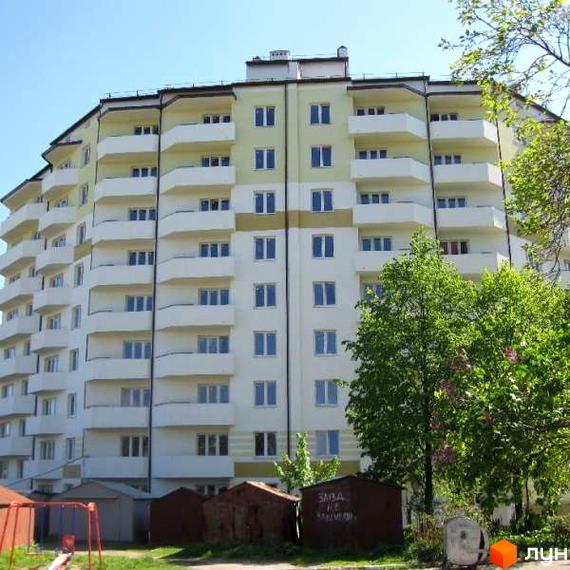 Зовнішній вигляд багатоповерхового житлового комплексу на вул. 50-річчя УПА, 10в, з численними балконами та світлими фасадами. На прибудинковій території видно зелені насадження та невеликі господарські споруди.