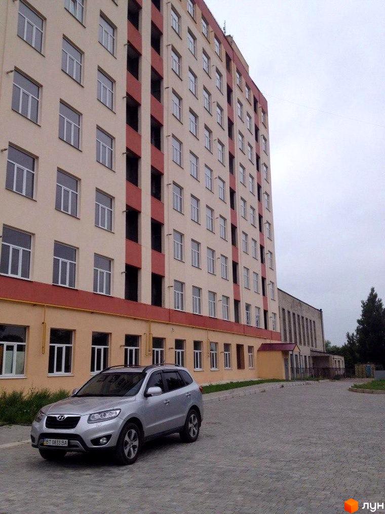 Зовнішній вигляд багатоповерхового будинку ЖК Сонячний Острів з червоними елементами фасаду та прибудинкова територія з автомобілем.