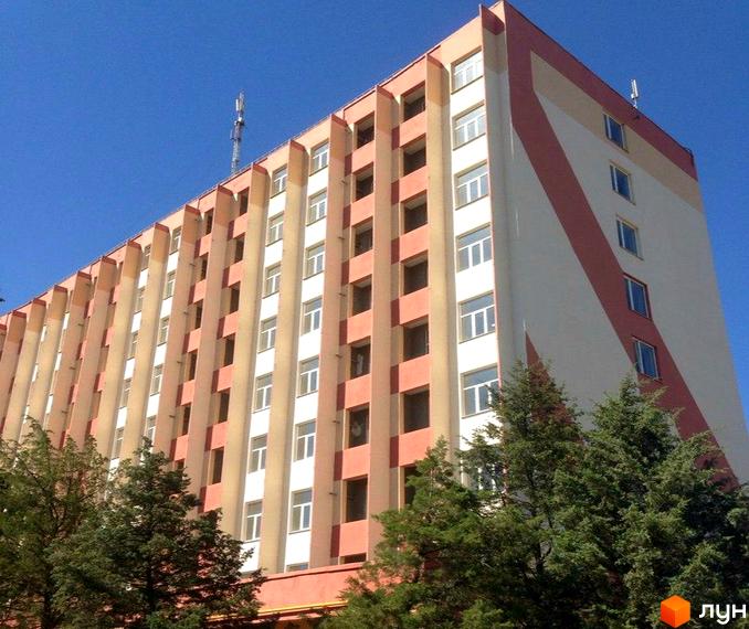 Зовнішній вигляд багатоповерхового будинку ЖК Сонячний Острів з фасадом у світлих тонах та декоративними елементами. Навколо будинку зелені дерева під чистим блакитним небом.
