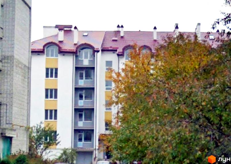 Житловий комплекс на вул. Величковского, 56а з білим фасадом, червоним дахом та жовтими акцентами. Перед будинком видно дерева з осіннім листям.