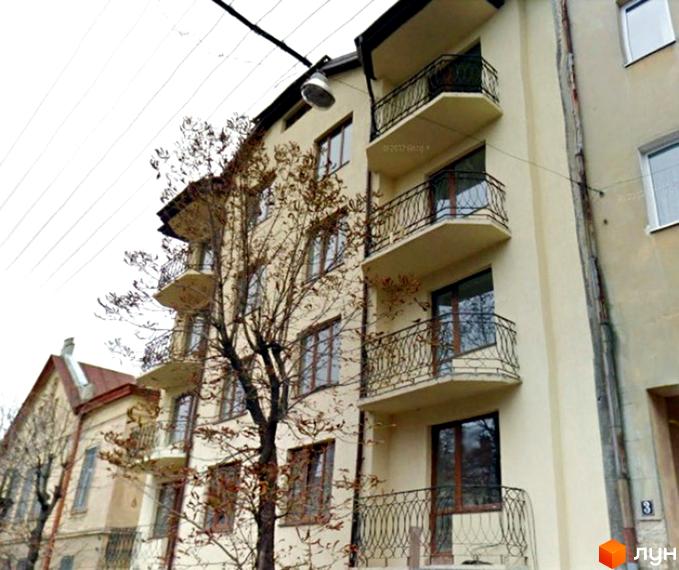 Фасад житлового будинку на вул. Максима Кривоноса, 3а: світлі стіни, коричневі вікна та балкони з кованими перилами. Поруч видно дерево.