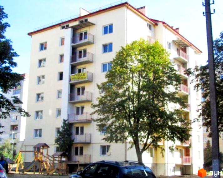 Новобудова на вул. Річицька, 9: багатоповерховий житловий будинок світлого кольору з балконами, поруч дитячий майданчик та зелені насадження.
