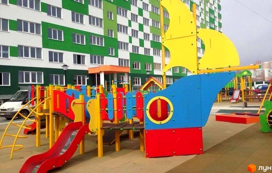Зовнішній вигляд будинку житлового комплексу ЖМ Острови з яскравими кольоровими елементами дитячого майданчика на прибудинковій території.