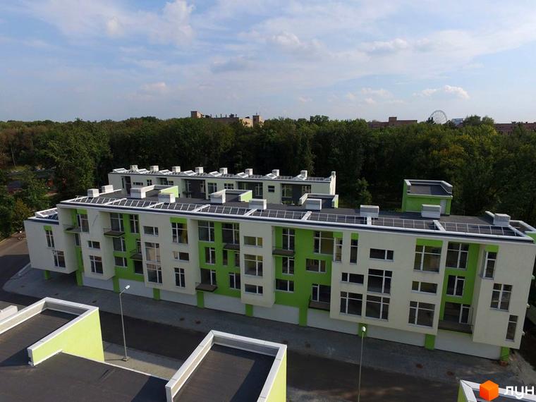 Зображення Житлового комплексу Shatilovka Hillside. Багатоповерховий будинок з зеленими вставками, сонячними панелями на даху та прибудинковою територією.