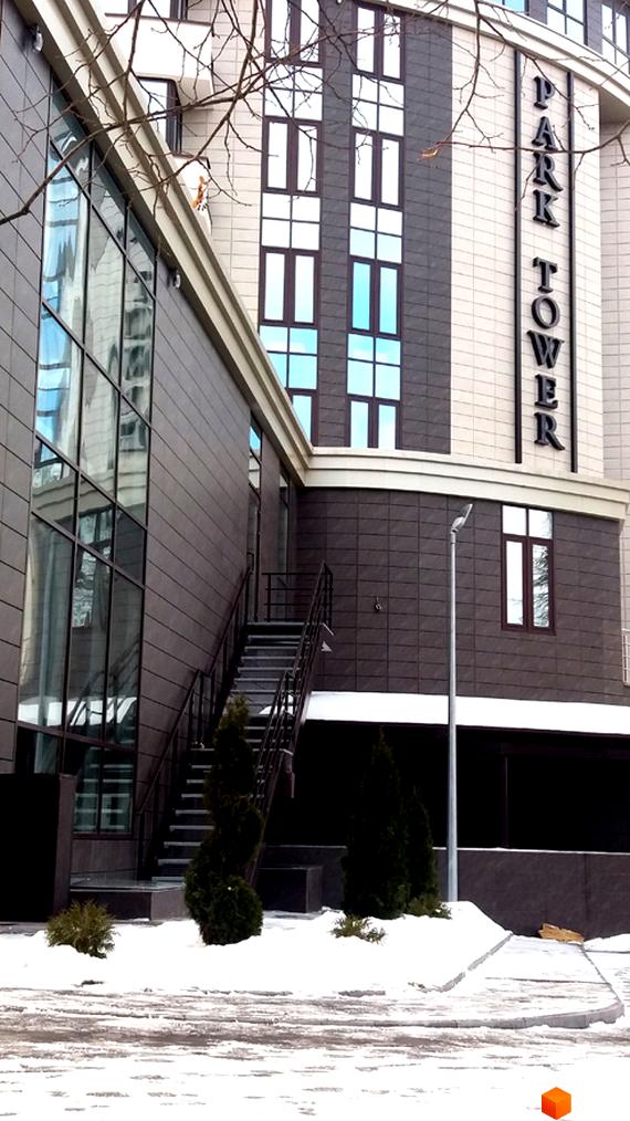 Зовнішній вигляд новобудови Park Tower з великими вікнами та сходами. Навколо будівлі засніжена територія з деревами.