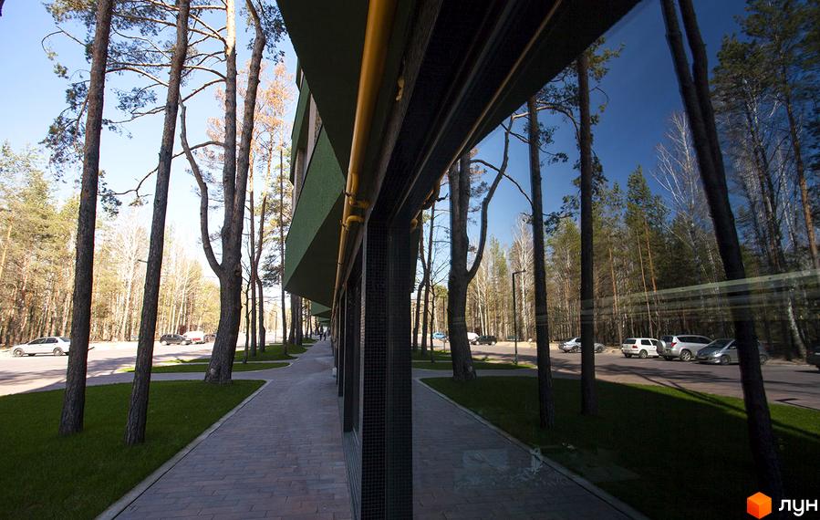 Зовнішній вигляд будівлі ЖК Park Town з великими вікнами та терасою. На передньому плані тротуарна доріжка та зелена трава, навколо високі дерева.