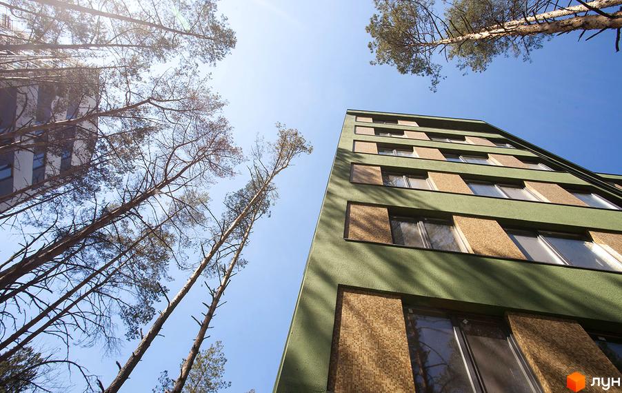 Висотна будівля ЖК Park Town з фасадом зеленого кольору та коричневими вставками. Навколо будинку ростуть високі дерева, сонячне світло освітлює фасад.