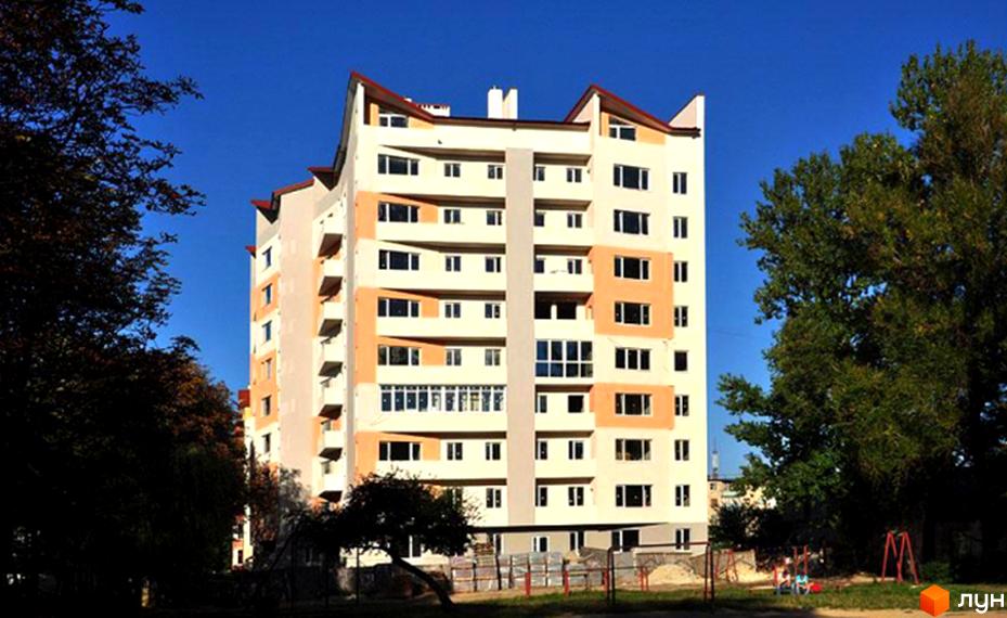 Житловий комплекс світлого кольору з помаранчевими вставками та хвилястим дахом. Поруч видно дерева та дитячий майданчик.