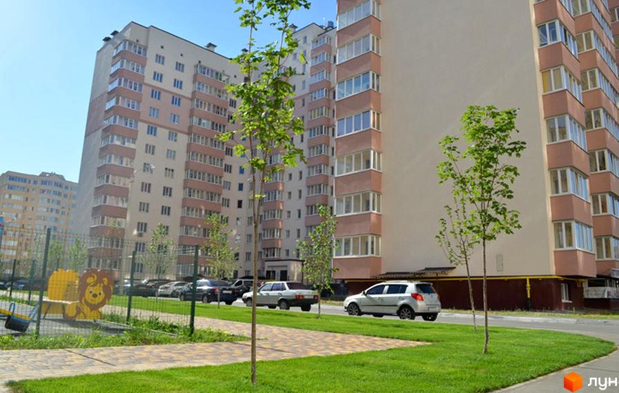 Житловий комплекс Софіївська Слобідка. Багатоповерхові будинки з балконами та великими вікнами, зелена прибудинкова територія з дитячим майданчиком та автомобілями.