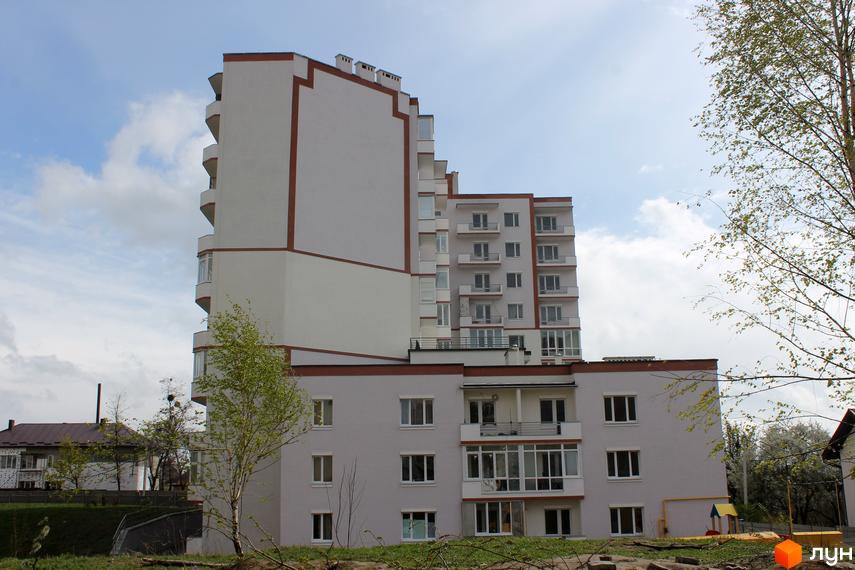 Новобудова на вул. Еммануїла Миська (Врубеля), 15. Багатоповерховий будинок світло-сірого кольору з коричневими елементами та балконами. Навколо зелена територія та дерева.