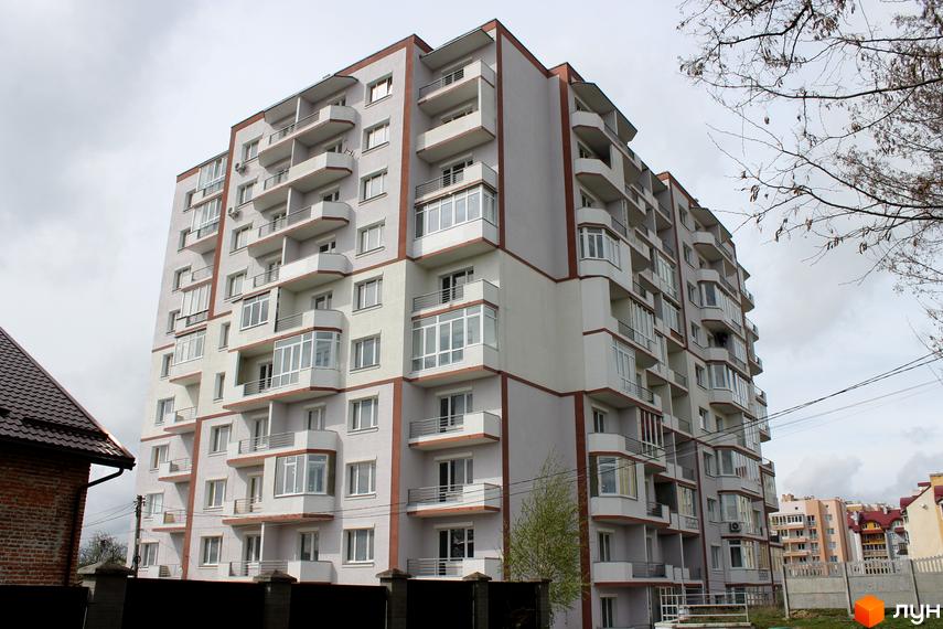 Багатоповерховий житловий комплекс на вулиці Еммануїла Миська (Врубеля), 15. Будинок має світло-сірий фасад з коричневими акцентами та численними балконами. Поруч видно паркан та дерева.