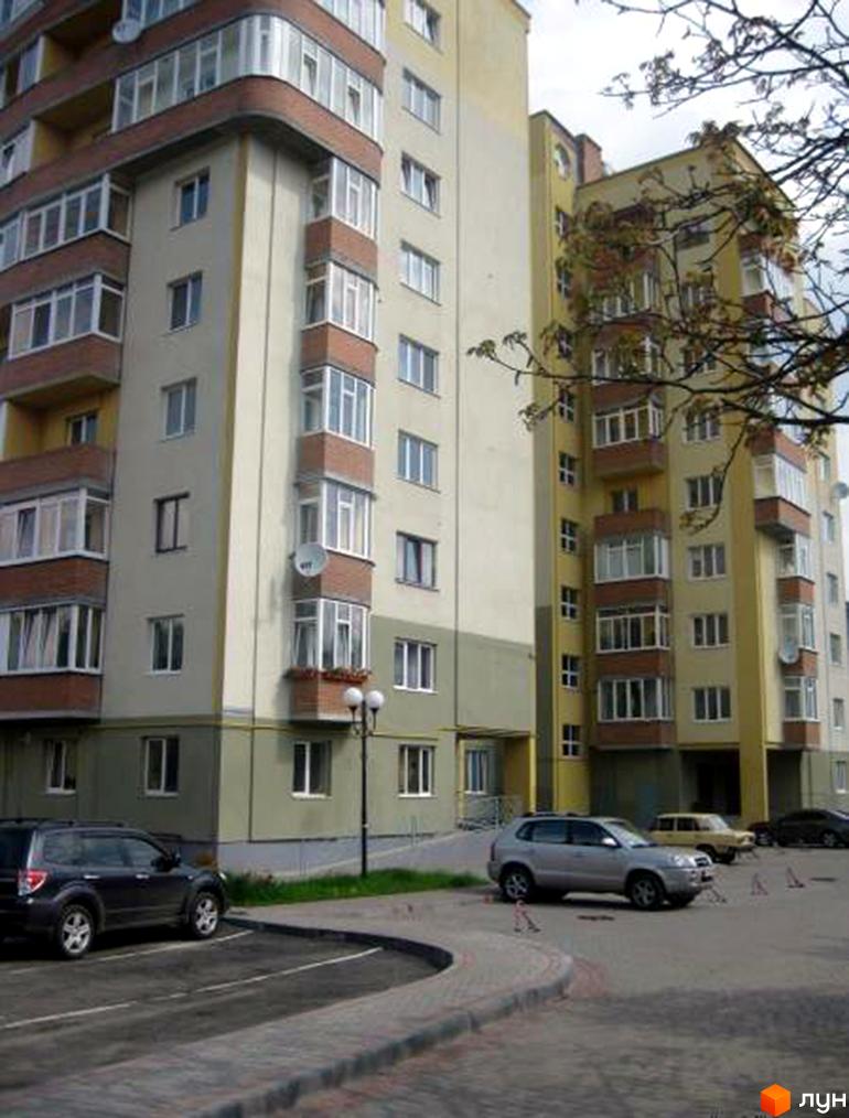 Багатоповерхові житлові будинки бежевих та сірих відтінків з заскленими балконами на вул. Караджича. На передньому плані парковка з автомобілями та пішохідна зона.